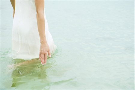 Woman standing knee deep in ocean, touching surface of water, cropped Stock Photo - Premium Royalty-Free, Code: 633-01715193