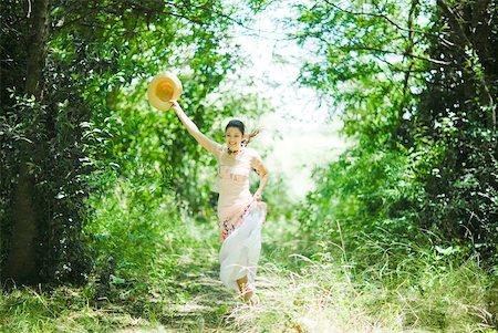 simsearch:633-01714195,k - Young woman in sundress running along wooded path, holding up sun hat Stock Photo - Premium Royalty-Free, Code: 633-01715214