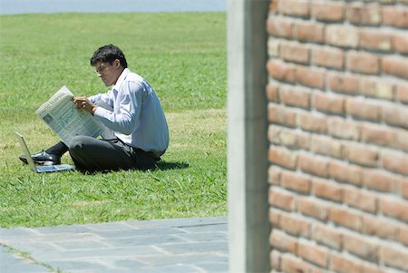 Businessman sitting on ground with laZSop, reading newspaper Stock Photo - Premium Royalty-Free, Code: 633-01715268