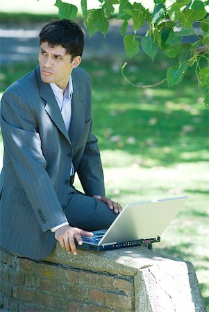 simsearch:633-01573622,k - Businessman sitting on low wall in park, using laZSop, looking away Fotografie stock - Premium Royalty-Free, Codice: 633-01715273