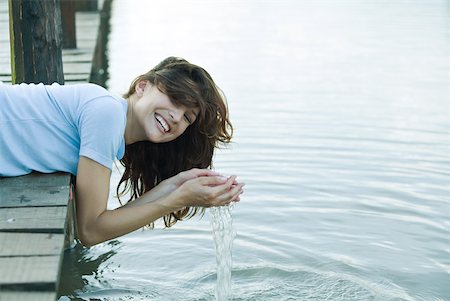 Woman leaning off edge of dock, holding water in cupped hands, laughing Stock Photo - Premium Royalty-Free, Code: 633-01715356