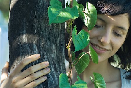 simsearch:633-01572737,k - Young woman holding onto tree trunk, smiling with eyes closed Foto de stock - Royalty Free Premium, Número: 633-01715403