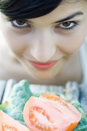 simsearch:633-01715082,k - Young woman leaning face over cut up tomatoes, smiling at camera, close-up Stock Photo - Premium Royalty-Free, Code: 633-01715510