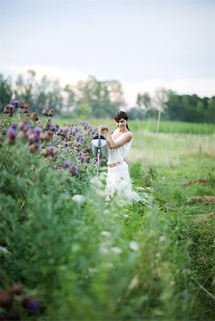 Young woman watering plants with watering can, in mid distance, smiling at camera Stock Photo - Premium Royalty-Free, Code: 633-01715512