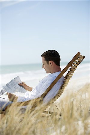 Man sitting in deckchair on beach, reading newspaper Stock Photo - Premium Royalty-Free, Code: 633-01715681