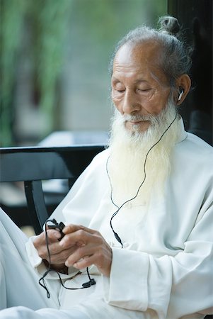 Elderly man in traditional Chinese clothing listening to MP3 player Stock Photo - Premium Royalty-Free, Code: 633-01715925
