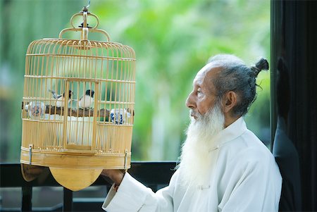 Elderly man in traditional Chinese clothing, looking at birds in bird cage Stock Photo - Premium Royalty-Free, Code: 633-01715927