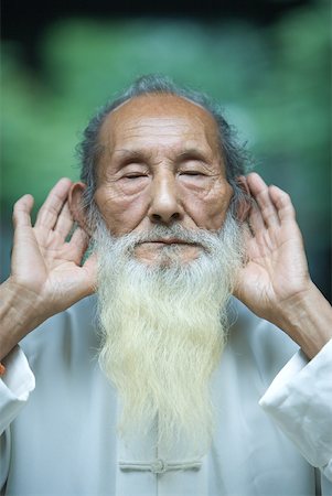 eyes closed portrait of asian man - Elderly man in traditional Chinese clothing holding hands behind ears Stock Photo - Premium Royalty-Free, Code: 633-01715938