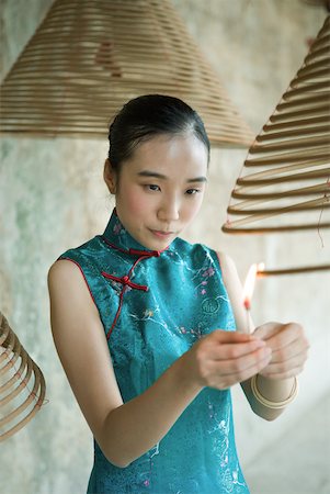 Young woman dressed in traditional Chinese clothing lighting spiral incense hanging from ceiling Stock Photo - Premium Royalty-Free, Code: 633-01715930