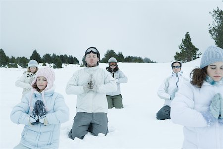 Groupe de jeunes amis à genoux dans la neige avec les mains jointes et les yeux fermés Photographie de stock - Premium Libres de Droits, Code: 633-01713711