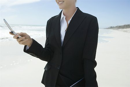 simsearch:633-01574593,k - Businesswoman holding cell phone, standing on beach, smiling, cropped Stock Photo - Premium Royalty-Free, Code: 633-01713766