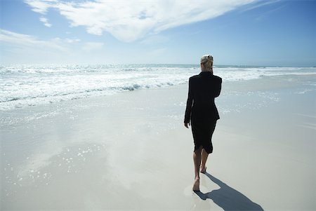 Businesswoman using cell phone, walking barefoot across beach, full length, rear view Stock Photo - Premium Royalty-Free, Code: 633-01713770