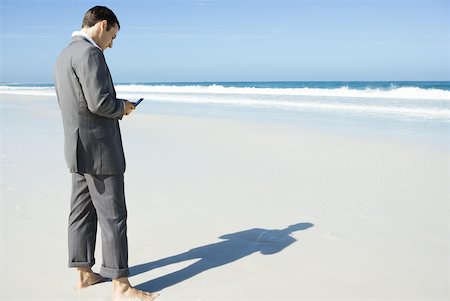 simsearch:633-01713789,k - Homme d'affaires pieds nus sur la plage, en regardant cell phone Photographie de stock - Premium Libres de Droits, Code: 633-01713796