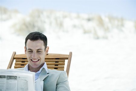Businessman sitting in deck chair at beach, reading newspaper, smiling Stock Photo - Premium Royalty-Free, Code: 633-01713828