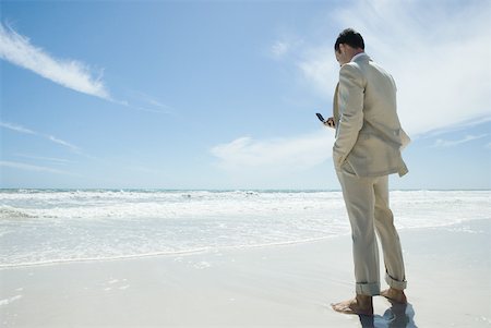 simsearch:633-01574593,k - Businessman standing barefoot on beach, holding cell phone Stock Photo - Premium Royalty-Free, Code: 633-01713858