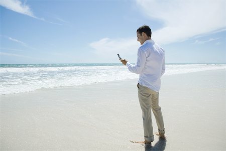 simsearch:633-01574593,k - Businessman standing barefoot on beach, holding up cell phone Stock Photo - Premium Royalty-Free, Code: 633-01713861