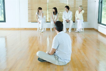 psicólogo - Man sitting on floor, facing group sitting in chairs Foto de stock - Royalty Free Premium, Número: 633-01713885