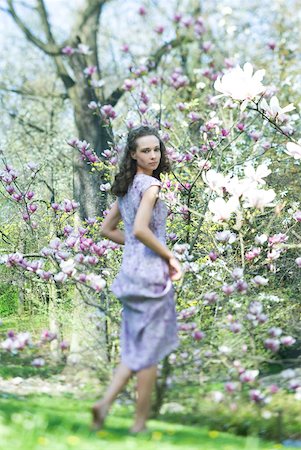 simsearch:633-01992711,k - Young woman in dress walking beside flowering tree, looking over shoulder at camera Stock Photo - Premium Royalty-Free, Code: 633-01837061