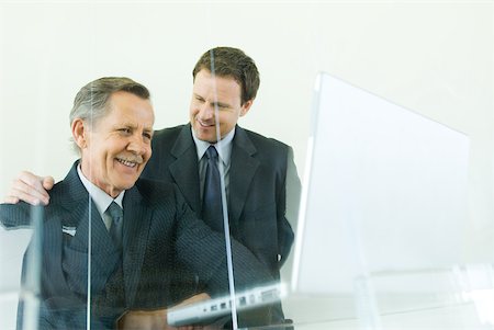 Two businessmen smiling together, one looking down at laZSop computer Stock Photo - Premium Royalty-Free, Code: 633-01837077