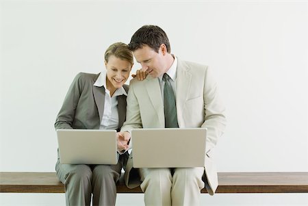 simsearch:695-03378944,k - Male and female business associates sitting side by side, both using laZSop computers, smiling Stock Photo - Premium Royalty-Free, Code: 633-01837081