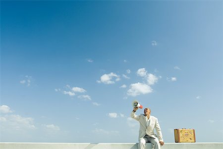 exile - Man sitting on wall beside suitcase, shouting into megaphone Stock Photo - Premium Royalty-Free, Code: 633-01837234