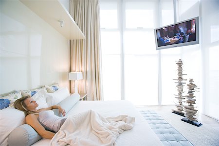 slacks women - Woman lying in bed watching widescreen TV in luxurious bedroom Stock Photo - Premium Royalty-Free, Code: 633-01992495