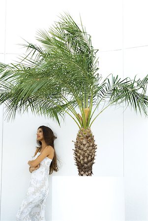 simsearch:695-03378068,k - Teen girl in dress with arms crossed, standing next to palm tree in planter, looking away Fotografie stock - Premium Royalty-Free, Codice: 633-01992543