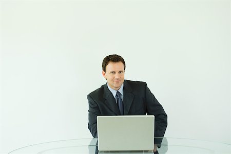 simsearch:633-02044233,k - Businessman sitting at desk, using laZSop computer, smiling at camera Stock Photo - Premium Royalty-Free, Code: 633-01992778