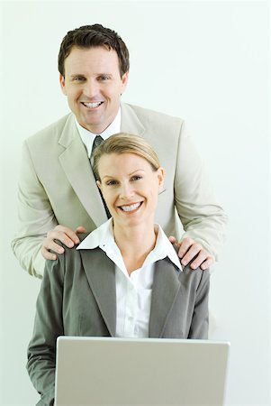 simsearch:633-02044233,k - Businessman standing behind female associate with his hands on her shoulders, both smiling at camera Stock Photo - Premium Royalty-Free, Code: 633-01992789