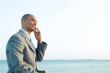 simsearch:632-01828543,k - Businessman by the sea using cell phone, smiling, side view Foto de stock - Royalty Free Premium, Número: 633-01992791