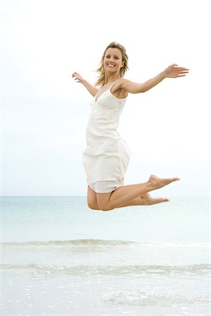 simsearch:633-01714473,k - Femme sautant en l'air à la plage, souriant à la caméra Photographie de stock - Premium Libres de Droits, Code: 633-02044406