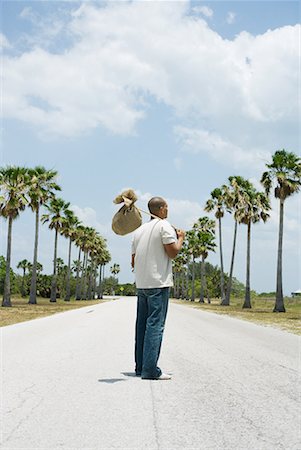 Man standing in middle of road, carrying burlap bundle on shoulder, rear view Foto de stock - Sin royalties Premium, Código: 633-02044609