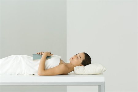 Woman lying on massage table, holding book on chest, eyes closed Stock Photo - Premium Royalty-Free, Code: 633-02128606