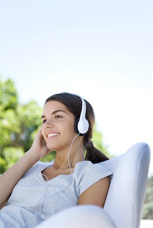 Woman listening to headphones outdoors, sitting in chair Stock Photo - Premium Royalty-Free, Code: 633-02128656
