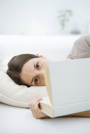 Woman lying on her side, smiling at camera, holding book partially in front of her face Stock Photo - Premium Royalty-Free, Code: 633-02128659