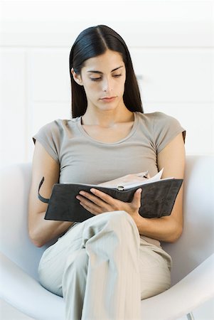 Woman sitting in chair, turning the page of her journal Stock Photo - Premium Royalty-Free, Code: 633-02128739