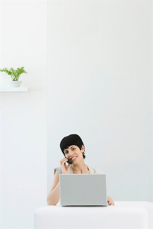 simsearch:633-02345800,k - Woman using laZSop computer and cell phone, smiling at camera Stock Photo - Premium Royalty-Free, Code: 633-02128747