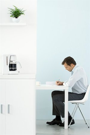 Man sitting at desk, working, coffee maker on counter in foreground Stock Photo - Premium Royalty-Free, Code: 633-02128748