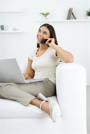 simsearch:632-02745019,k - Woman sitting on sofa, talking on cell phone, looking away, holding laZSop Stock Photo - Premium Royalty-Free, Code: 633-02128757
