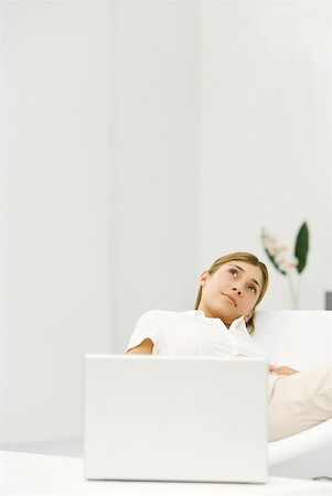 simsearch:632-02345008,k - Woman reclining in chair beside laZSop computer, looking up, smiling Stock Photo - Premium Royalty-Free, Code: 633-02128801