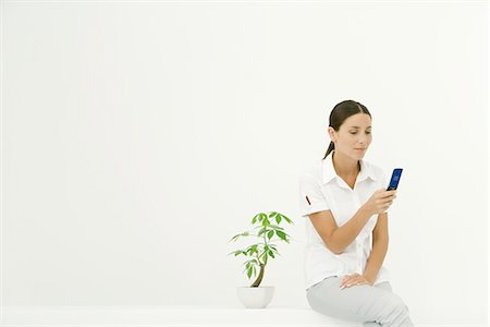 simsearch:632-01271195,k - Woman sitting beside potted plant, using cell phone Fotografie stock - Premium Royalty-Free, Codice: 633-02231700