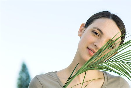 simsearch:633-02345793,k - Young woman with palm leaf, smiling at camera Stock Photo - Premium Royalty-Free, Code: 633-02231736