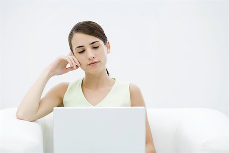 simsearch:633-02345800,k - Young female sitting in armchair, leaning on elbow, looking down at laZSop computer Stock Photo - Premium Royalty-Free, Code: 633-02345789