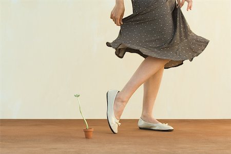 Woman walking past tiny potted plant, holding skirt, cropped view Stock Photo - Premium Royalty-Free, Code: 633-02345924