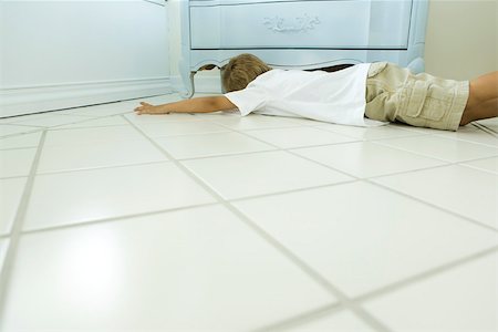 Boy lying on floor, looking under chest of drawers Stock Photo - Premium Royalty-Free, Code: 633-02417931