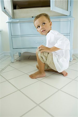 Boy crouching beside open armoire, looking over shoulder Stock Photo - Premium Royalty-Free, Code: 633-02417933