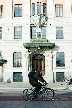 side view of a guy riding a bike - Sweden, Stockholm, bicyclists riding past ornate building Stock Photo - Premium Royalty-Free, Code: 633-02691354