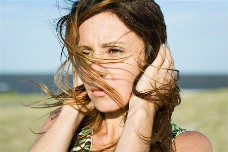 furrowed brow - Woman standing in wind, hands holding hair down, close-up Stock Photo - Premium Royalty-Free, Code: 633-03194712