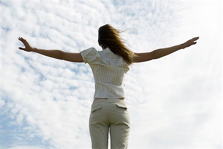 Woman with arms outstretched, cloudy sky in background, rear view Stock Photo - Premium Royalty-Free, Code: 633-03194800