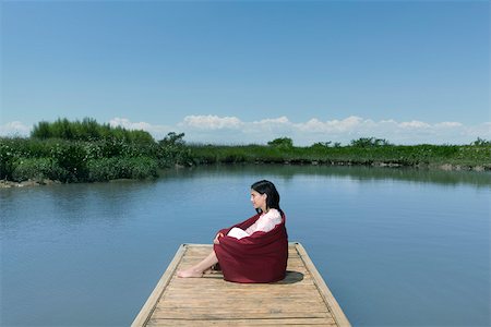 Woman sitting on dock with blanket wrapped around her, looking away in thought Stock Photo - Premium Royalty-Free, Code: 633-03444722